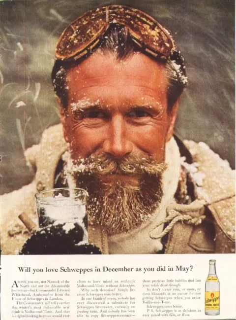 Ritratto del Commander Edward Whitehead, con barba e occhiali da sci, un bicchiere di Schweppes in mano