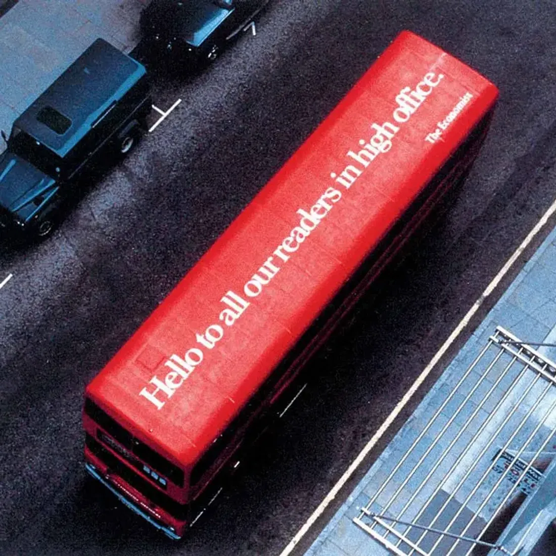 Un autobus londinese a due piani, ripreso dall'alto, con la scritta bianca su fondo rosso «Hello to all our readers in high office» sul tetto