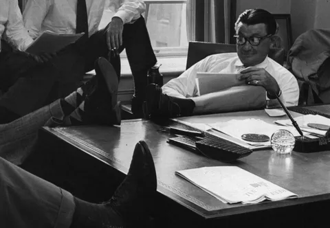 Fotografia d'epoca di alcuni uomini in ufficio con i piedi appoggiati sulla scrivania, in una pausa tra una riunione e l'altra: il lato meno formale del mestiere di convincere.